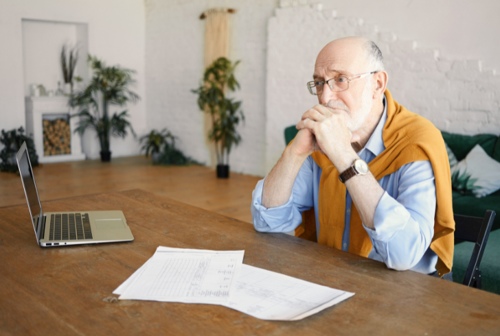 Elderly man looks worried while checking financial papers at home.